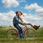 couple riding bike through field